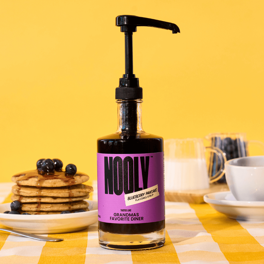 Blueberry Coffee Syrup bottle next to a plate of blueberry pancakes on a yellow tablecloth