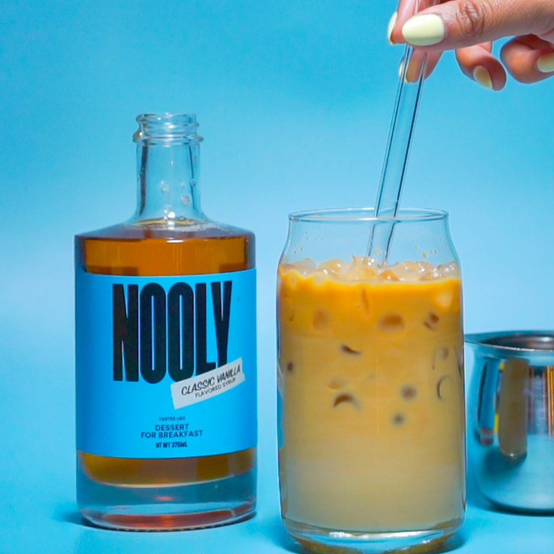 person stirring a vanilla latte next to a bottle of healthy vanilla syrup for coffee