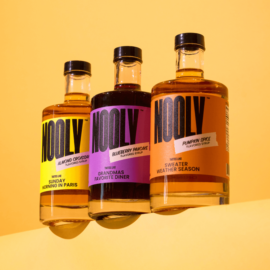 three different Nooly coffee syrup flavors lined up next to each other on a ledge with a pale yellow background
