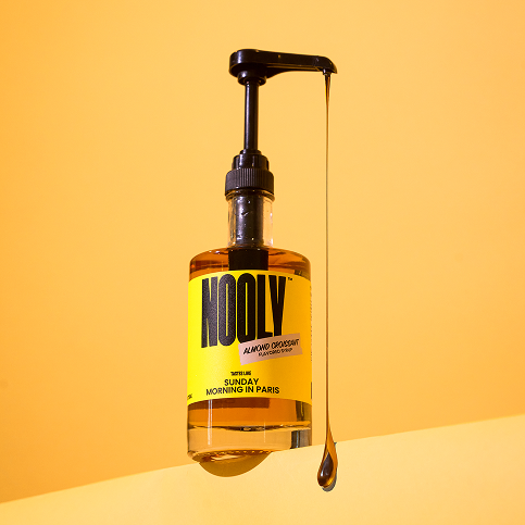 Nooly almond coffee syrup bottle with a long drip of almond syrup coming out of pump attachment