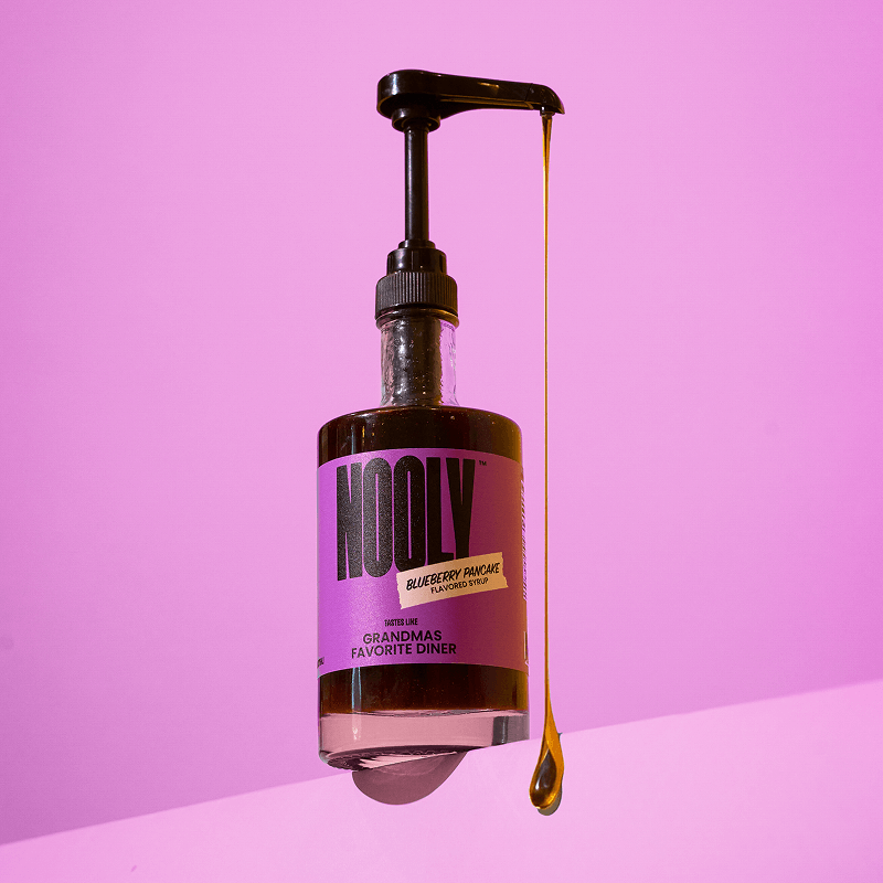 Bottle of Nooly blueberry coffee syrup with a long drip of blueberry syrup coming out of the pump attachment