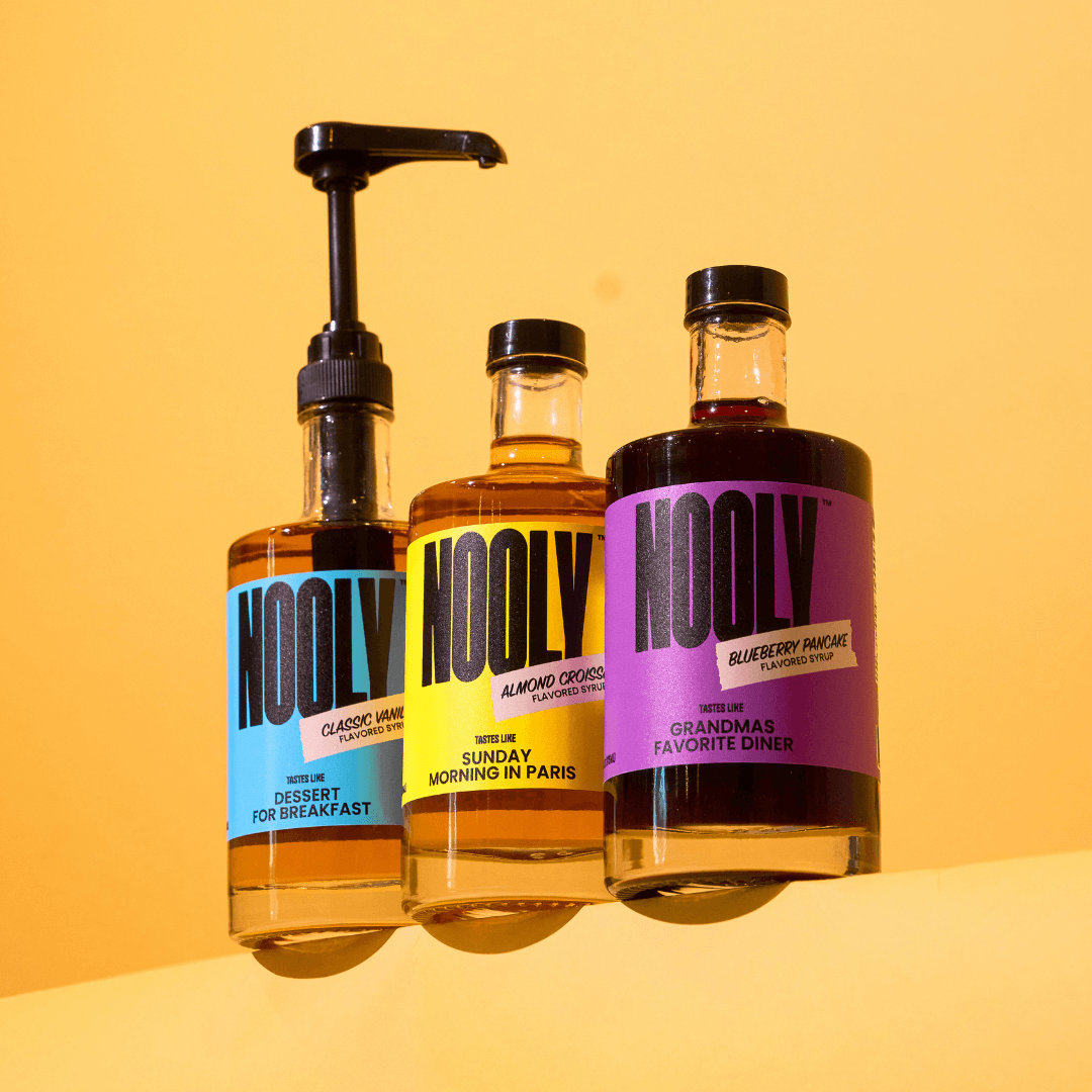 three bottles of Nooly coffee syrup with a syrup dispenser pump attached to the far left bottle