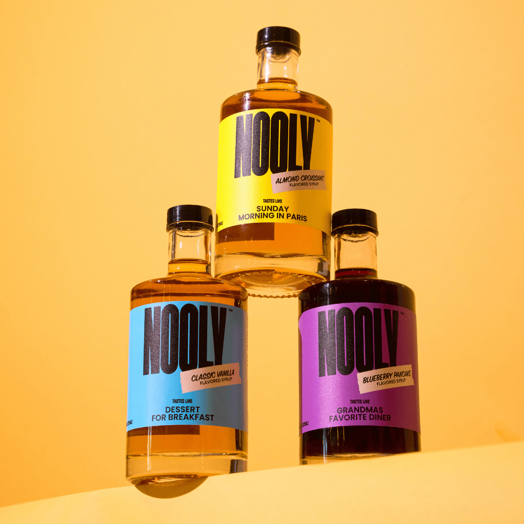 three bottles of Nooly syrup on a pastel orange background