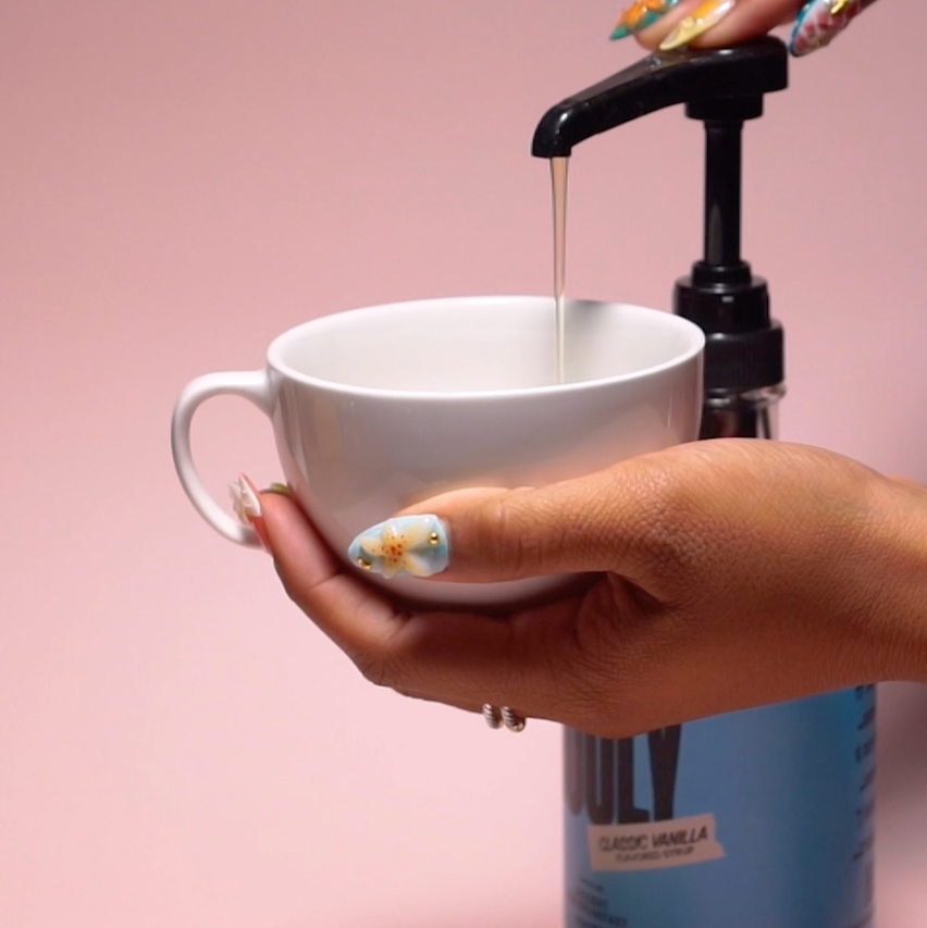 hand pressing syrup pumps into a coffee mug